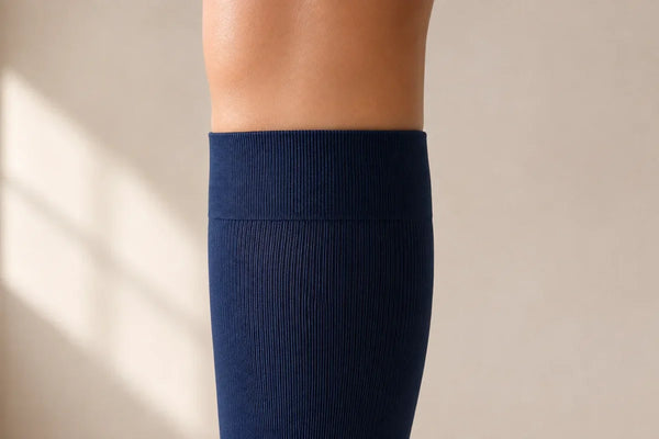 Side view of the flat top band of a navy knee-high compression sock on a standing leg, with even skin above it