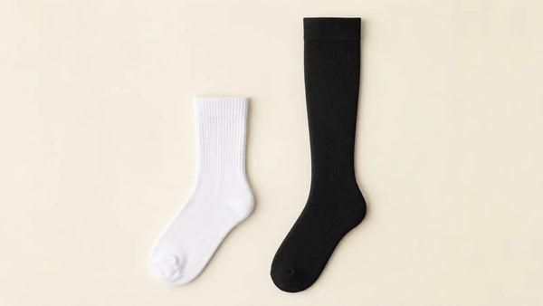 A white cotton crew sock laid next to a black knee-high graduated compression sock for comparison