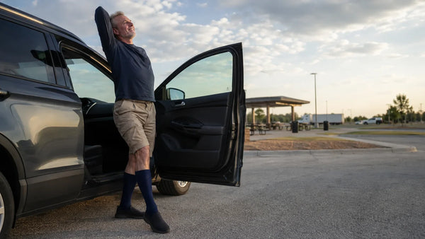 Man stretching beside an open car door at a highway rest stop, navy knee-high compression socks visible