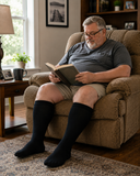 Man wearing black plus size wide calf compression socks while reading at home